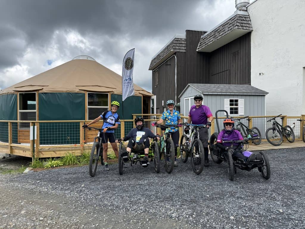 Six people stand infront of a yurt at Bolton Valley with their mountain bikes.